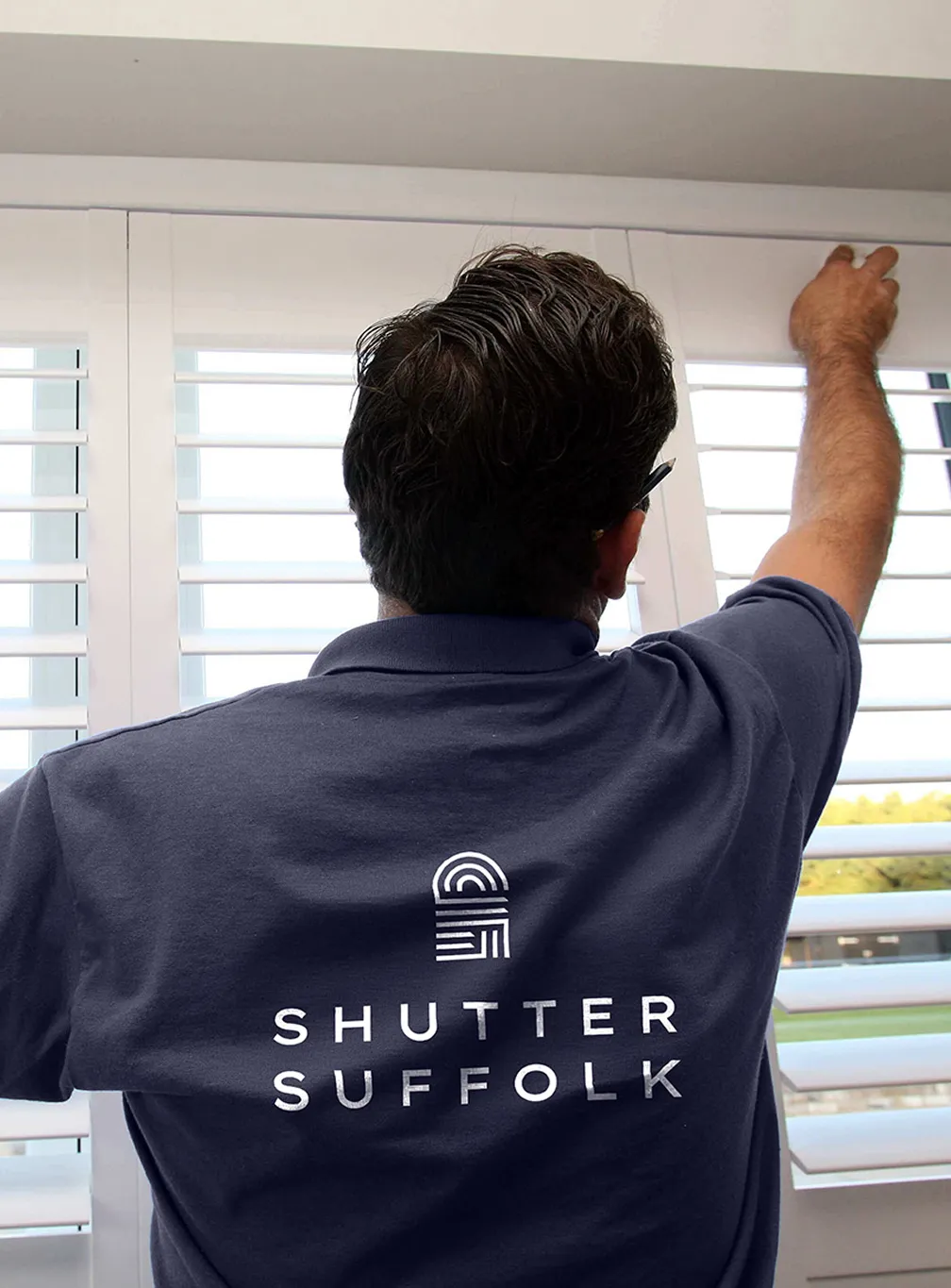 A Shutter Suffolk installer wearing a professional company shirt prominently displaying the updated logo across the back.