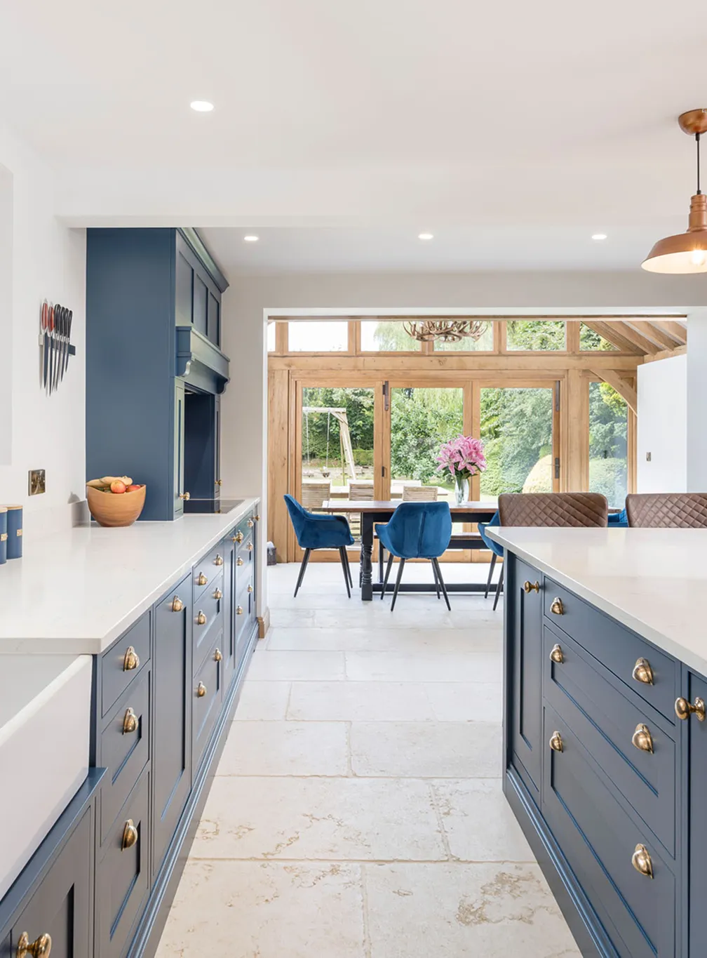 A bright, open-plan traditional shaker kitchen featuring elegant brass hardware accents and an integrated dining area by Burton Bespoke.