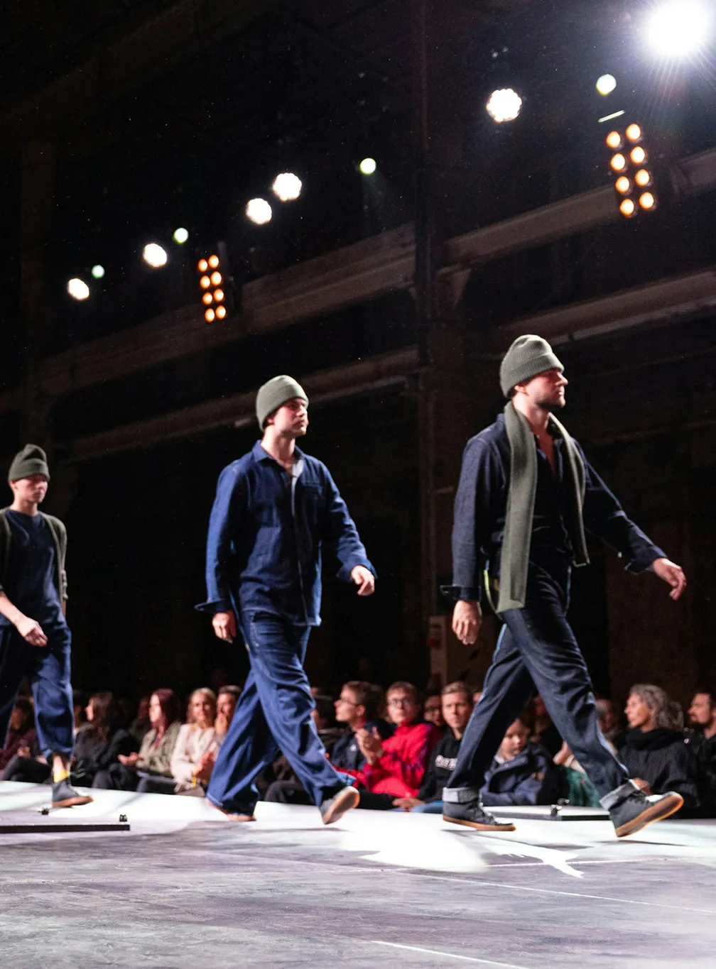 High-fashion lifestyle photography showcasing male models walking down a runway during a contemporary fashion show.