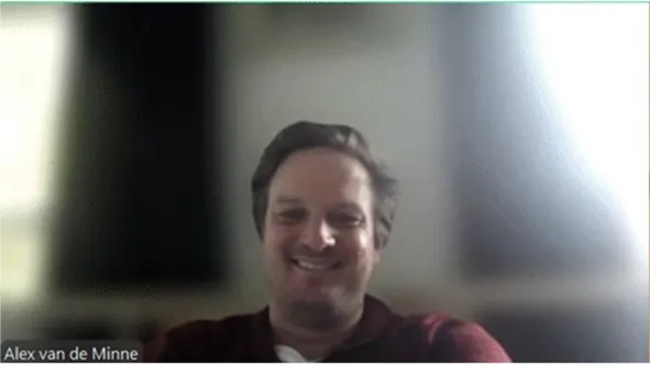 Alex van de Minne smiling during a video call, seated in a dimly lit room with soft natural light in the background.