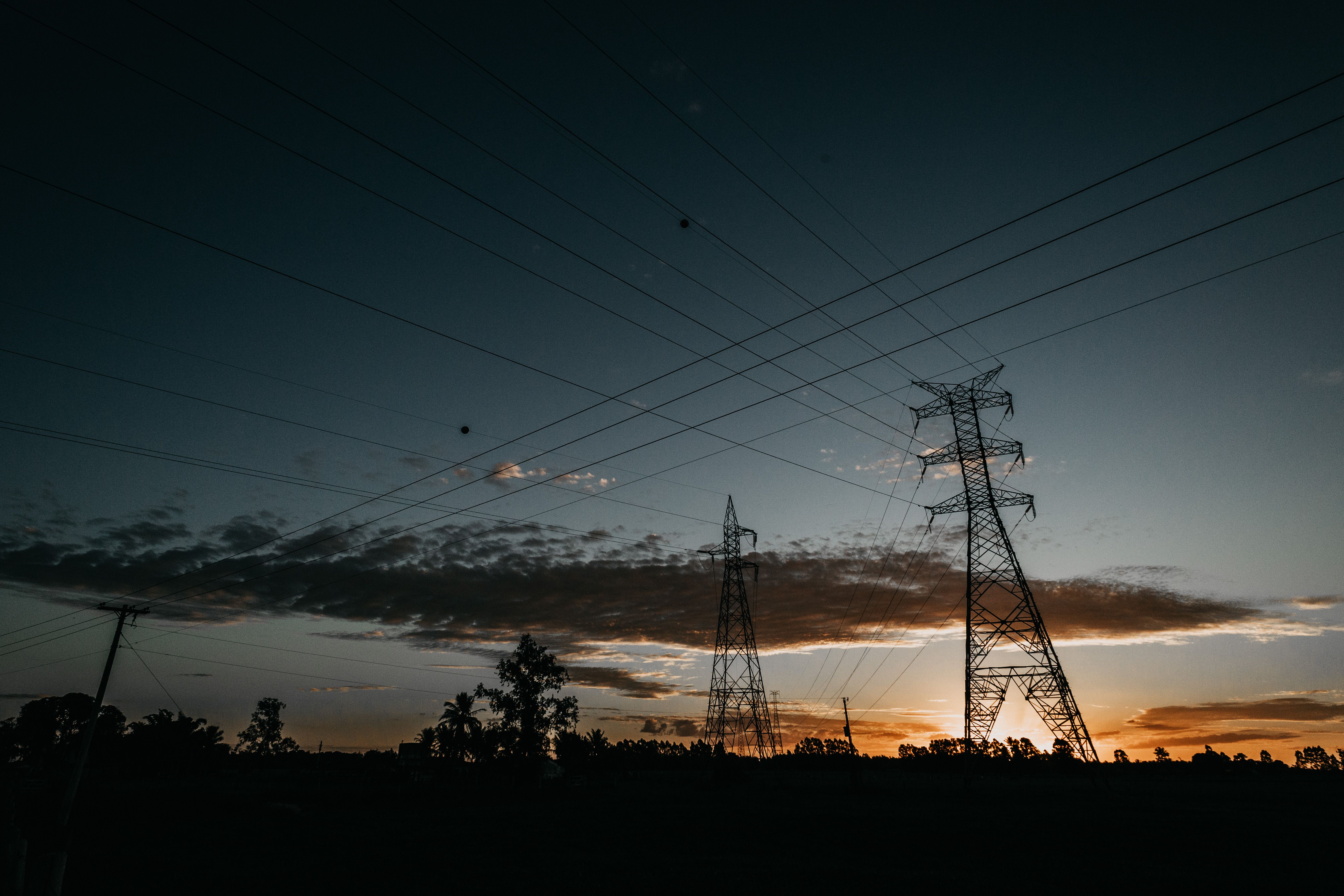 High voltage transmission lines silhouetted at dusk, the grid infrastructure homes choose to lean on or reduce reliance on with solar and batteries.