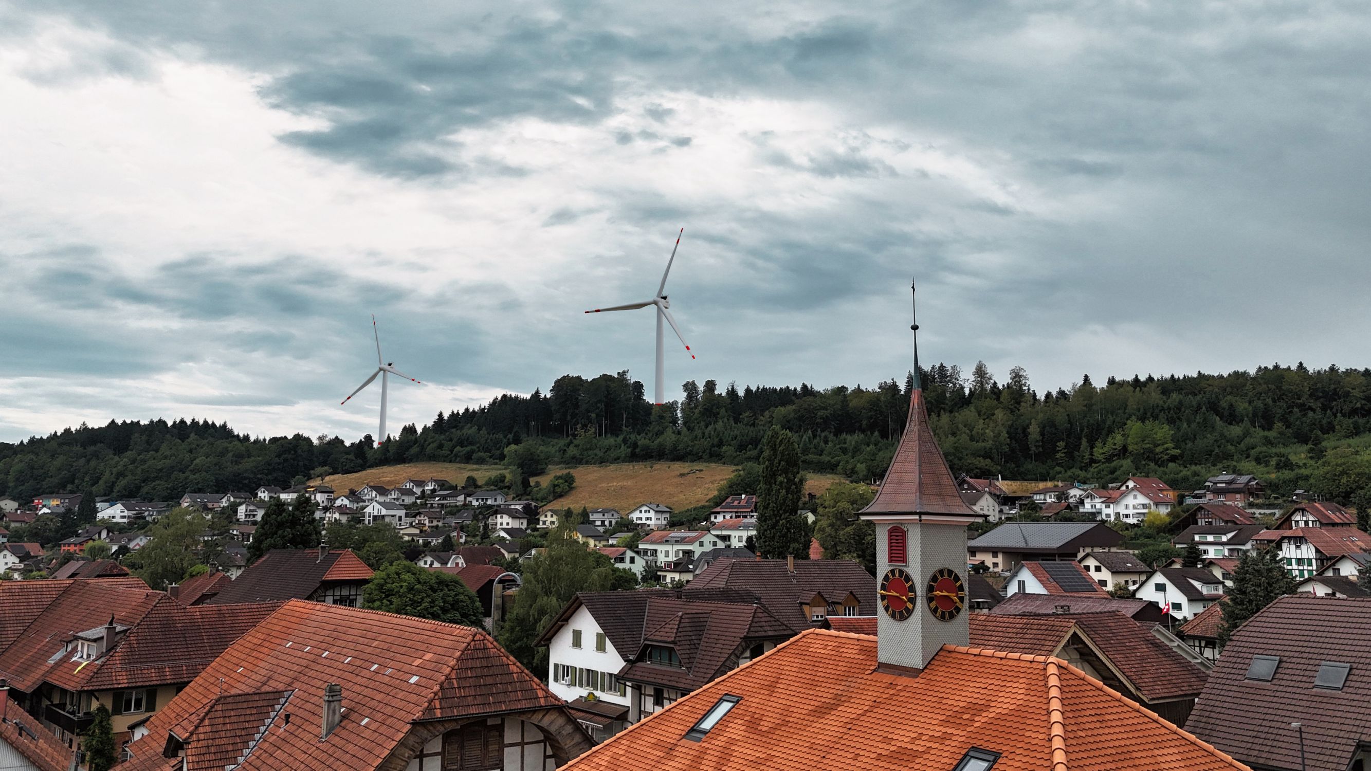 Windkraftnlage auf dem Hügel eines Dorfs. Die Bürger besitzen die Anlagen und partizipieren an jeder Umdrehung. Visualisierte Windanlagen auf echter Aufnahme einer Ortschaft.