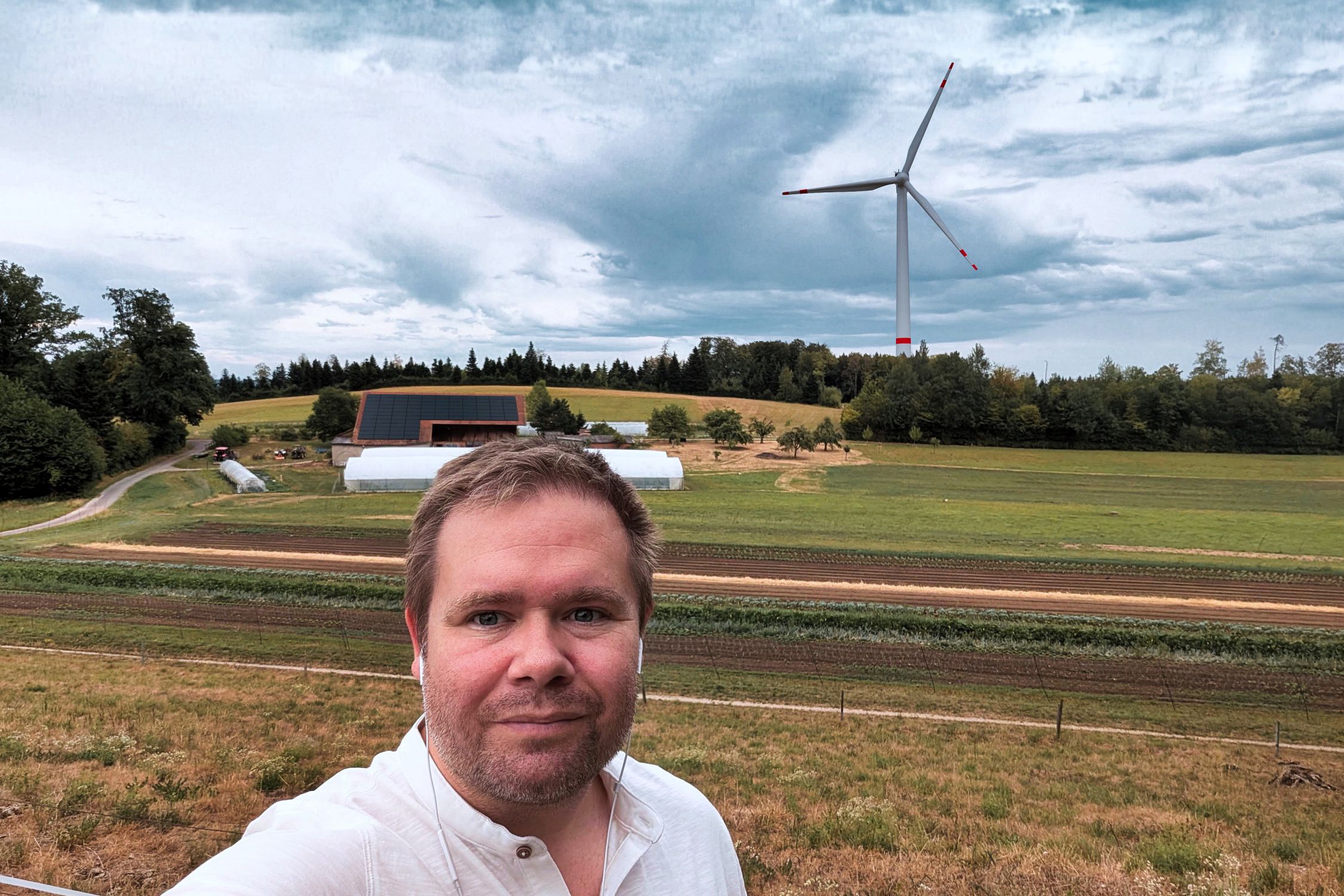 Selfie von Samuel Schneider, im Hintergrund Solaranlage auf dem Dach vom Hof und Windanlage visualisiert