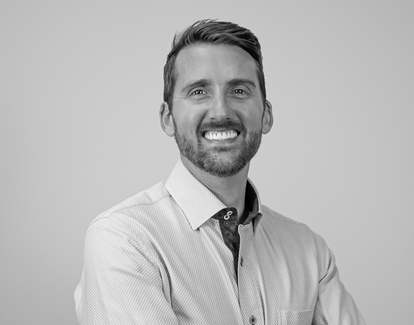 Black-and-white professional portrait of Steven Harp, Founder and CEO of Colorado Wealth Group. He is smiling confidently with his arms crossed, wearing a light-colored dress shirt with a patterned inner collar. His short hair is neatly styled, and he has a well-groomed beard. The background is a plain light gray, keeping the focus on him.