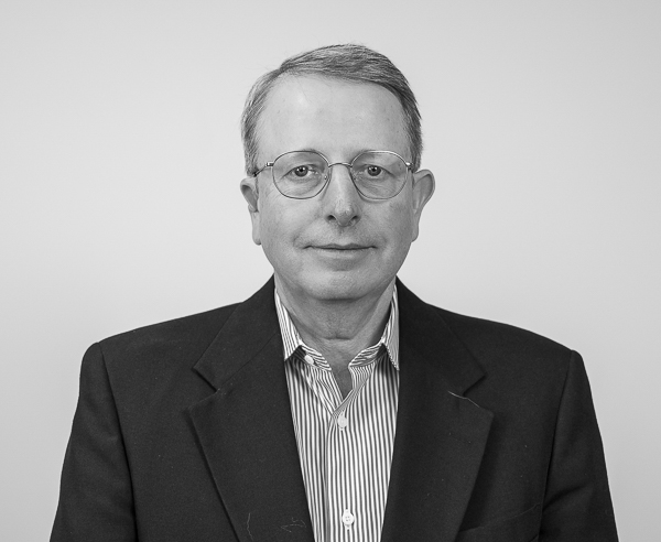 Black-and-white headshot of Bruce Larsen, Senior Wealth Advisor at Colorado Wealth Group. He is wearing glasses, a dark blazer over a button-down shirt, and has a neutral expression. His short hair is neatly combed, and the background is plain and light-colored, giving the portrait a professional tone.