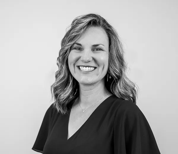 Black-and-white professional portrait of Emily Murtaugh, Director of Operations at Colorado Wealth Group. She is smiling warmly, wearing a dark V-neck blouse. Her medium-length wavy hair is styled loosely, and she stands against a plain, light background, creating a polished and approachable appearance.