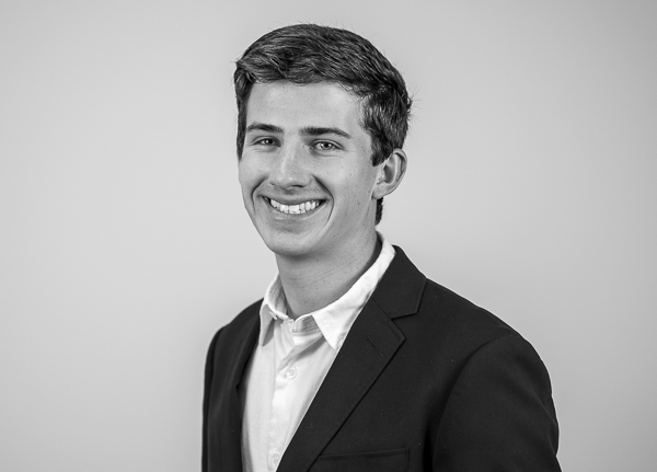 Black-and-white headshot of Carter Hench, Director of Financial Planning at Colorado Wealth Group. He is smiling subtly and wearing a dark suit jacket over a light-colored dress shirt. His hair is neatly styled, and he stands at a slight angle against a plain, light background, presenting a polished and professional appearance.