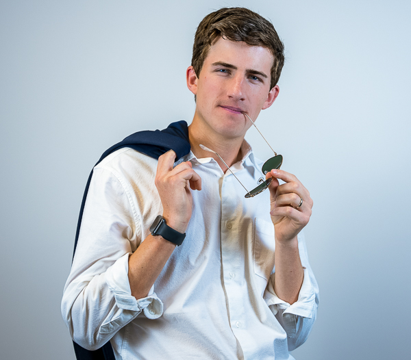 Carter Hench, Director of Financial Planning at Colorado Wealth Group, posing confidently with a jacket slung over his shoulder and holding sunglasses, dressed in a casual white shirt.