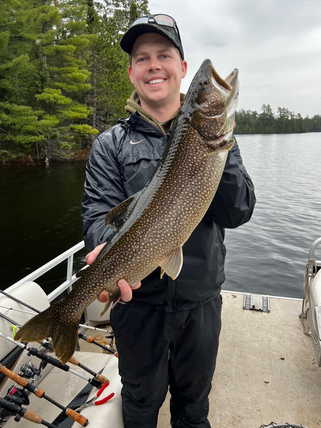 Ian Snedden, Head of Tax & Accounting at Colorado Wealth Group, smiling while proudly holding a large fish on a boat, dressed in outdoor gear with a lake and forest in the background.