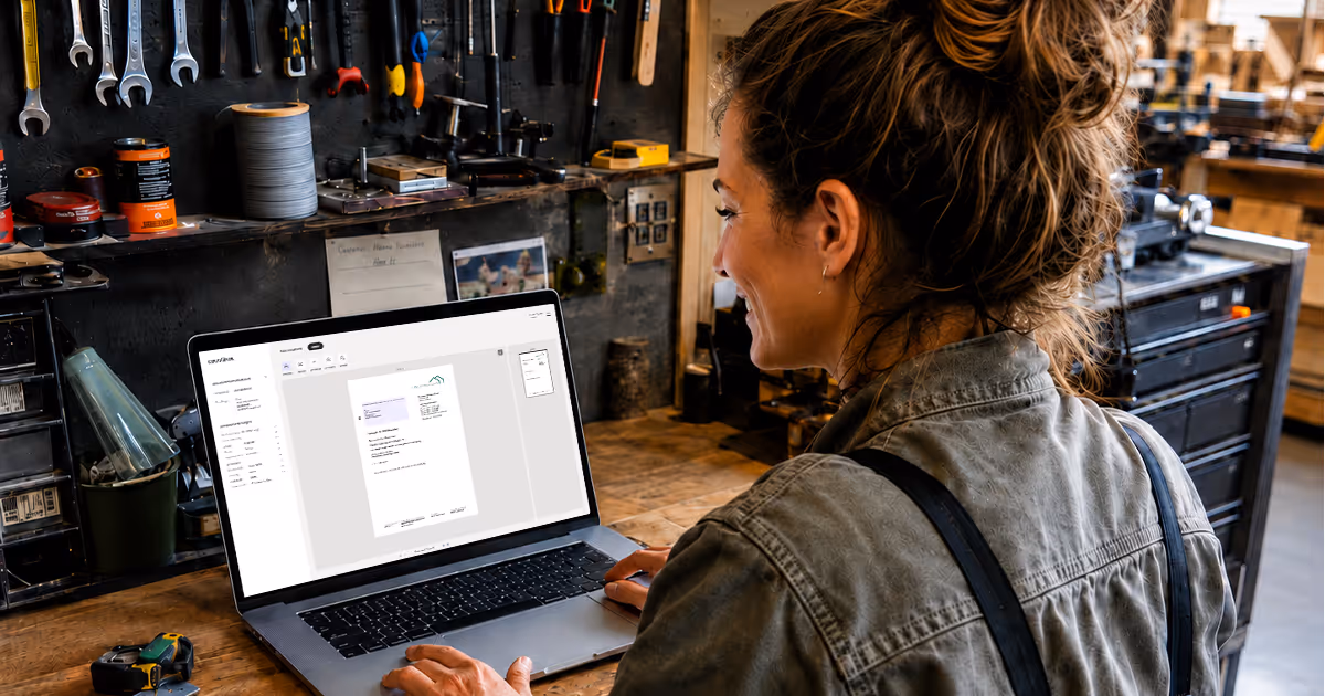 Eine SHK-Handwerkerin sitzt in Ihrer Werkstatt vor ihrem Laptop umgeben von Werkzeug und versendet Ihre Rechnungen bequem über die epostbox und spart sich den Weg zur Post