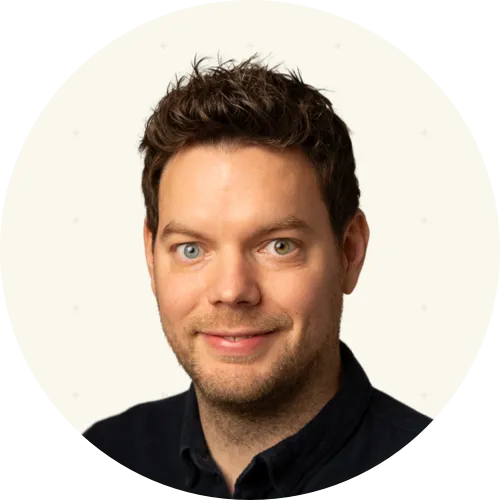 Portrait of a man with curly brown hair, wearing a dark shirt, and having heterochromia with one blue eye and one hazel eye.