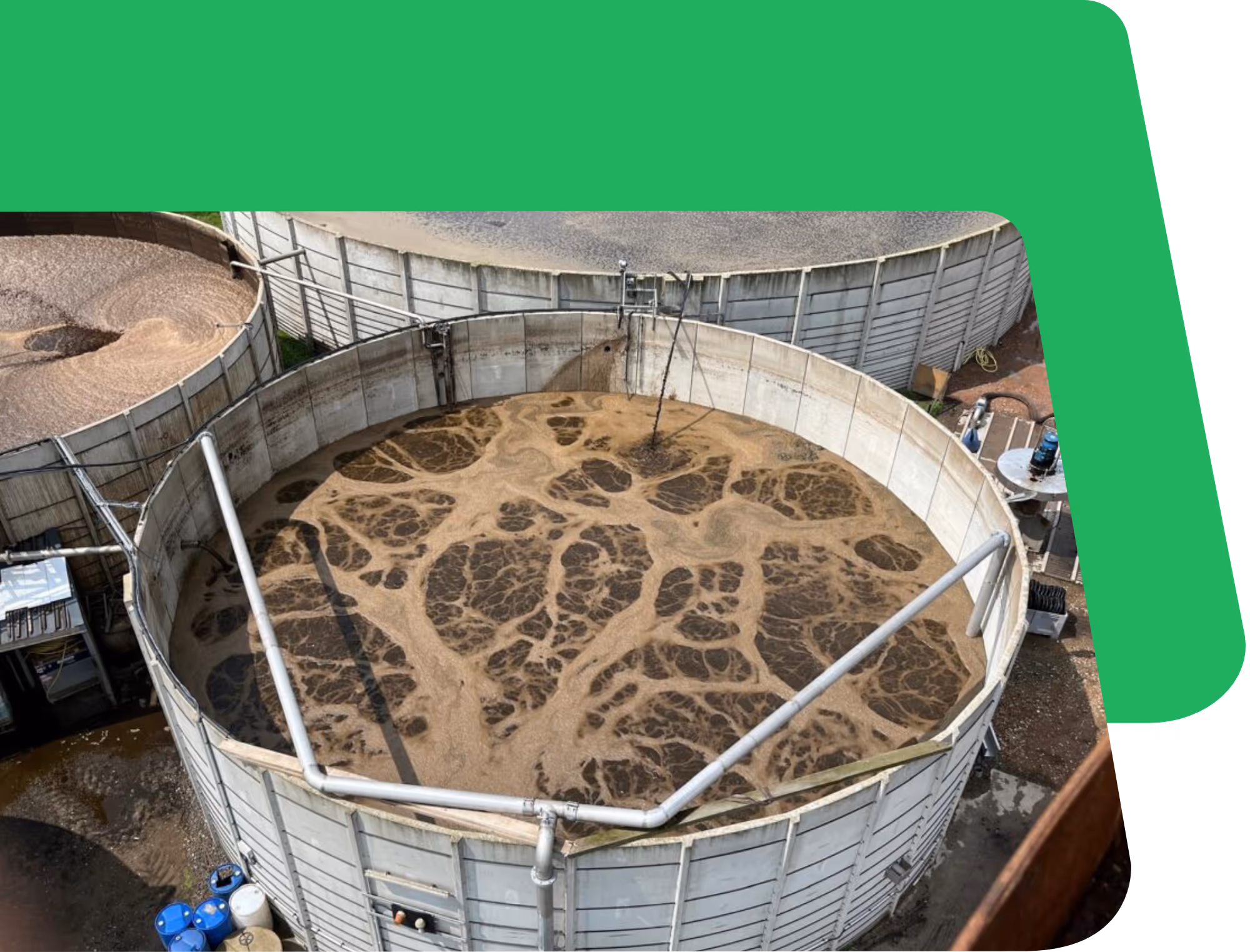 Bovenaanzicht van een ronde, industriële tank gevuld met wervelende donkerbruine vloeistof, die lijkt op gisting. De tank is omgeven door leidingen en metalen constructies.