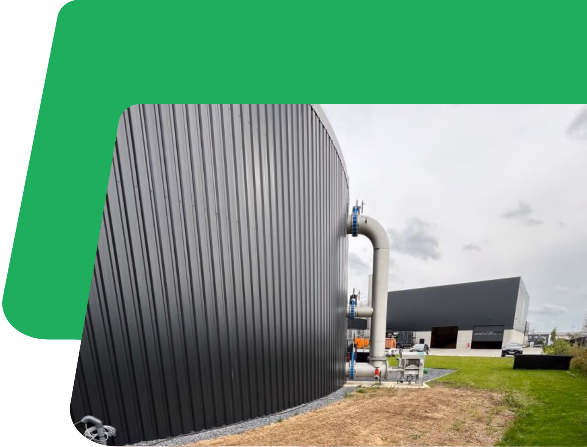 Grote industriële opslagtank met verticale ribbels en aangrenzende leidingen in een moderne faciliteit. Groen gras en grind omringen het gebied. De bewolkte lucht zorgt voor een functionele sfeer.