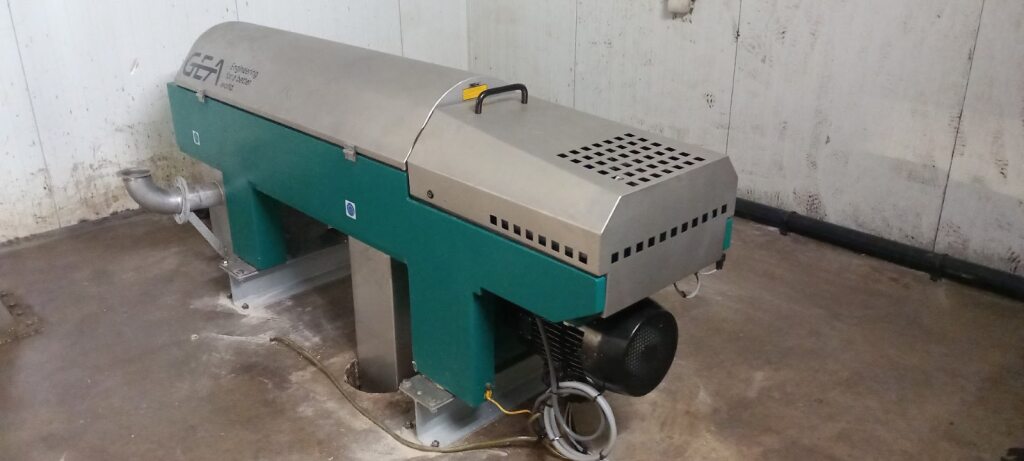 Grote industriële opslagtank met verticale ribbels en aangrenzende leidingen in een moderne faciliteit. Groen gras en grind omringen het gebied. De bewolkte lucht zorgt voor een functionele sfeer.