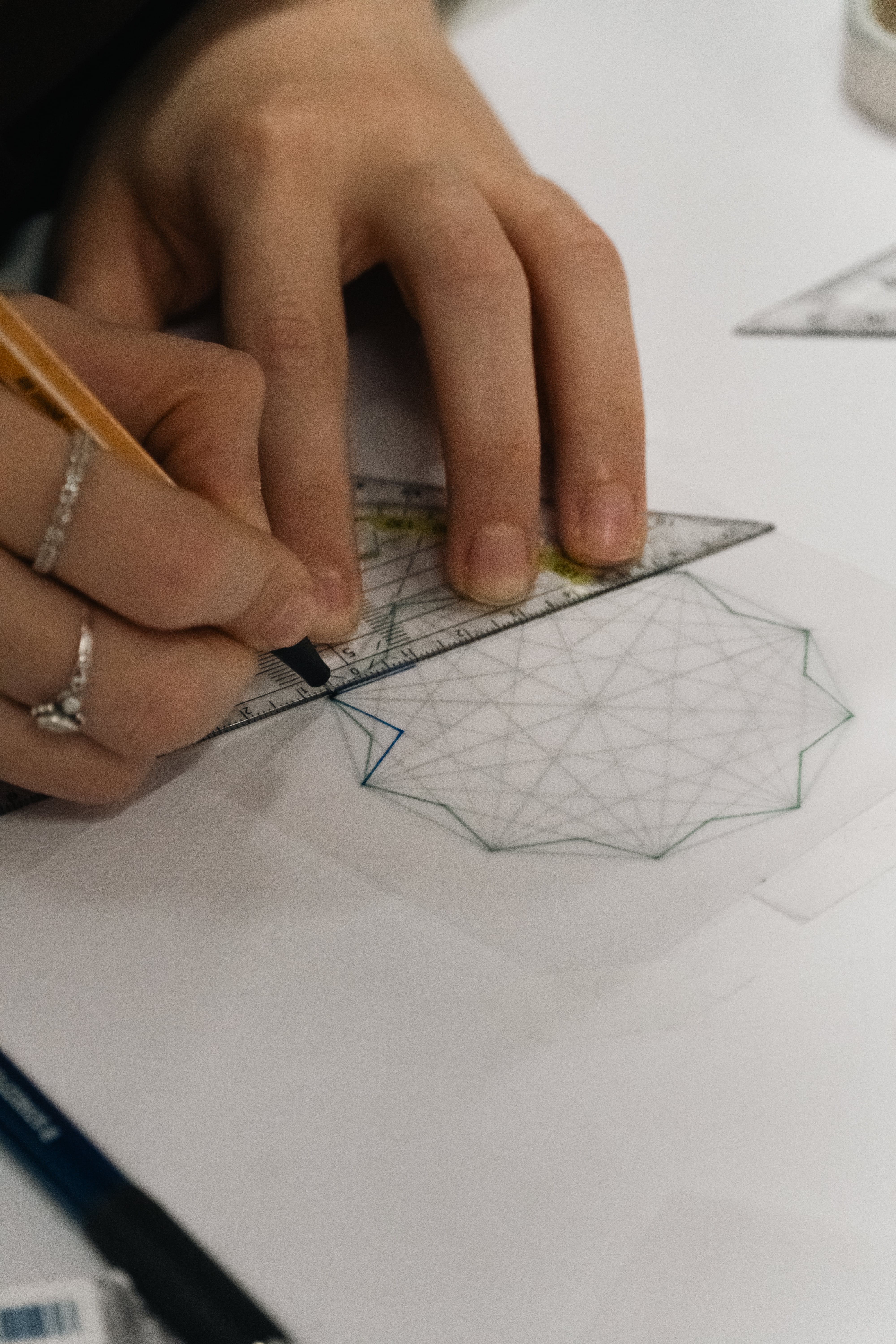 Close-up of hands using a ruler and pen to draw a geometric pattern on translucent paper.