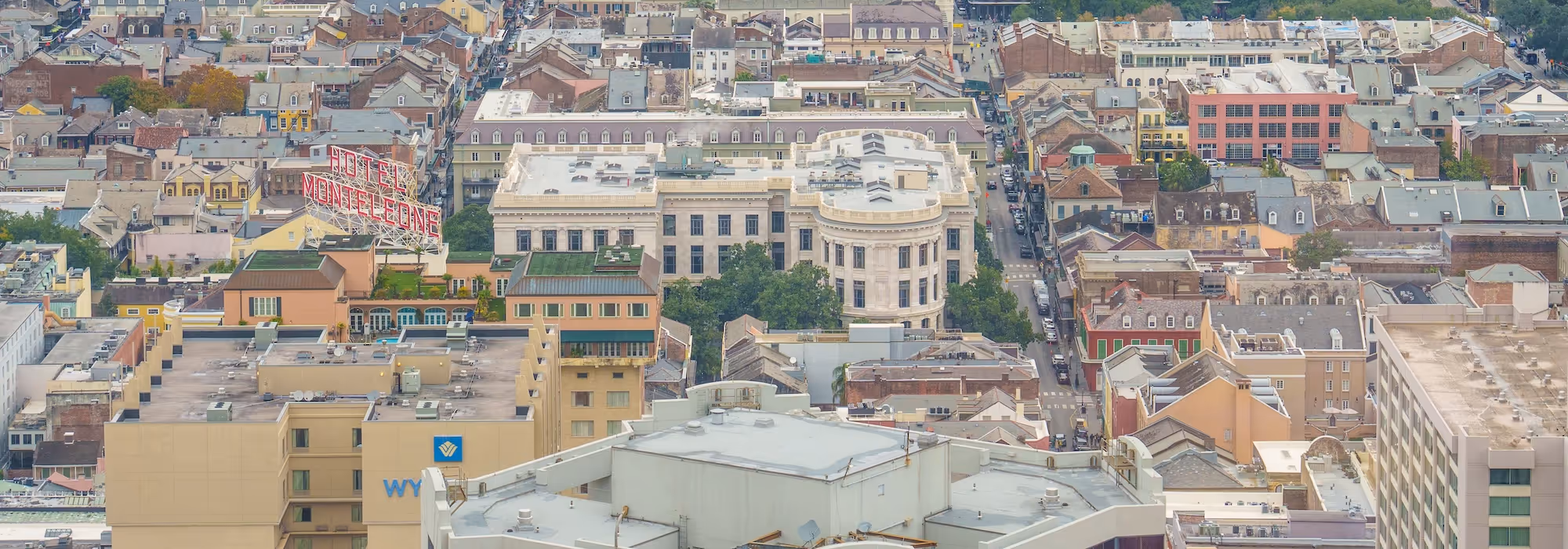 Aerial view of urban buildings with a prominent red neon sign reading 'HOTEL MONTELEONE' among tightly packed rooftops and streets.