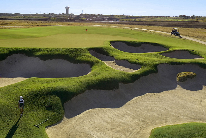 Golf course green with multiple deep sand bunkers and a golfer walking nearby.