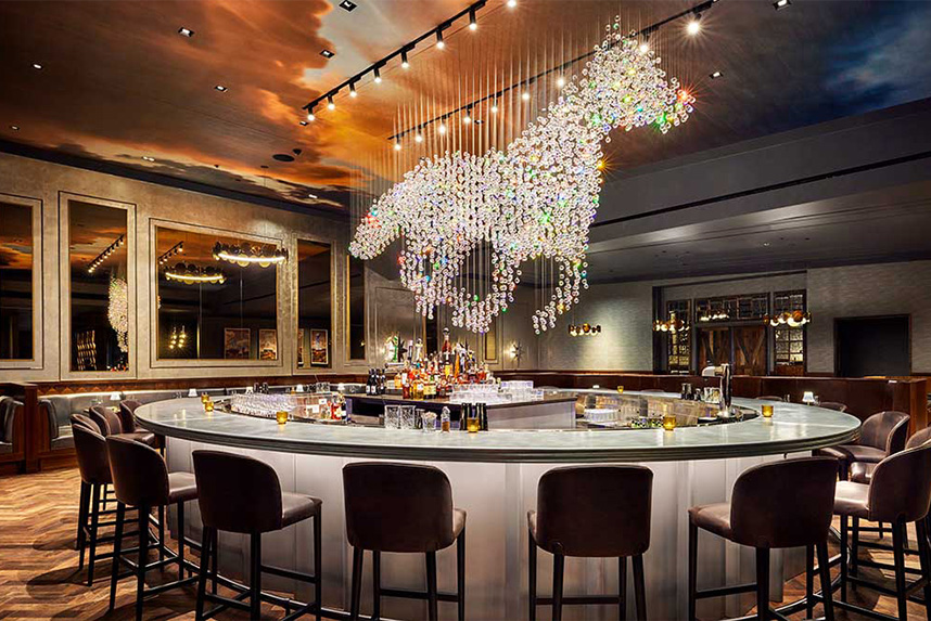 Upscale bar area with round marble counter and a large horse-shaped light fixture hanging above it.