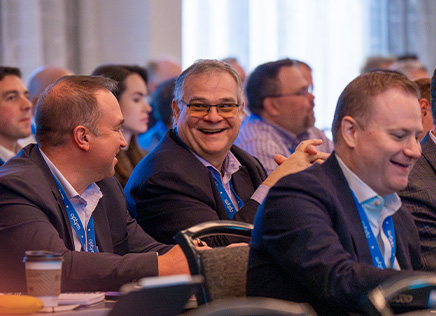 Group of business people wearing conference badges, chatting and smiling indoors.