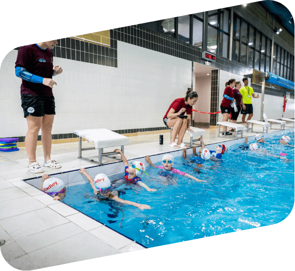A swim teacher talking to children in the swimming pool