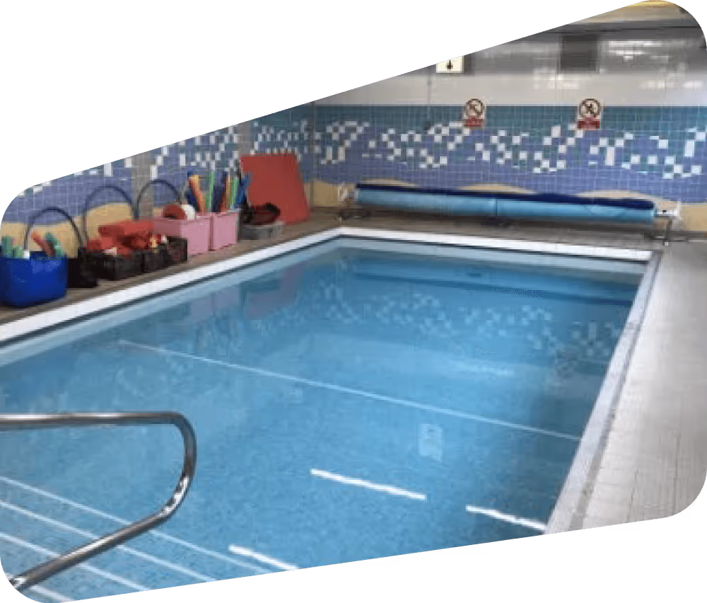Small indoor pool with blue water, handrail, swim equipment on the side, and no diving signs on the tiled wall.
