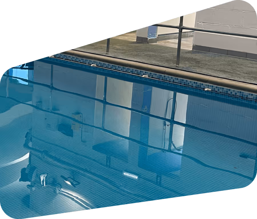 Reflection of a room with chairs and railing in a calm indoor swimming pool’s water.