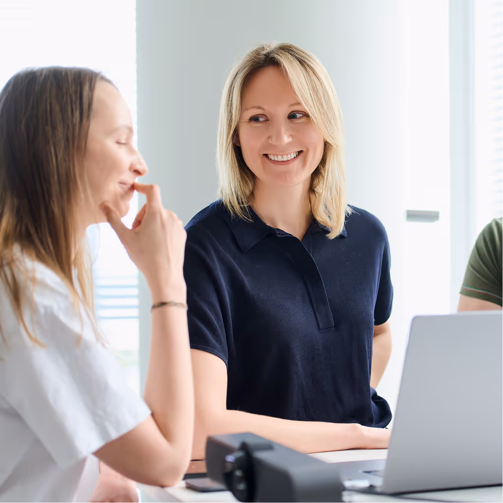 Two persons working at the desk with laptops and smiling to each other.