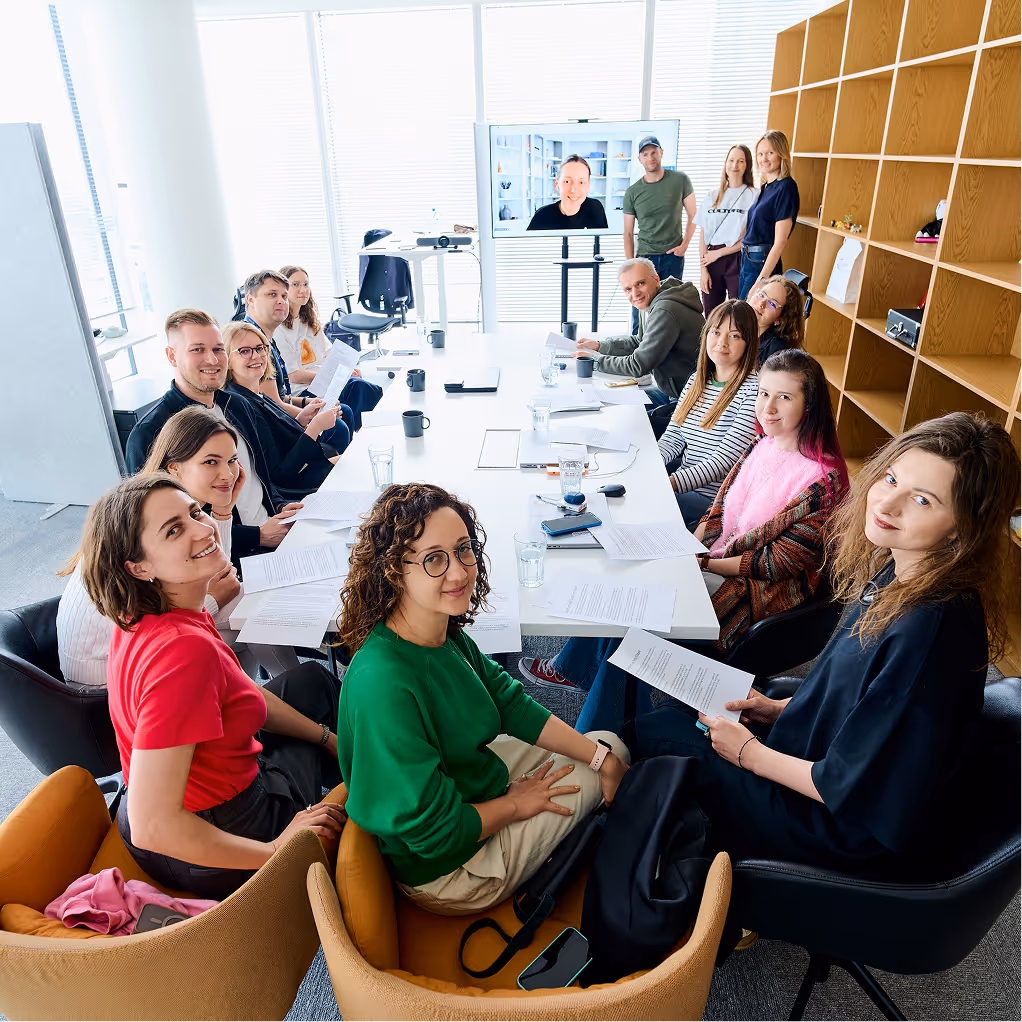 Group of smiling designers from the Norm team, sitting at the long table.