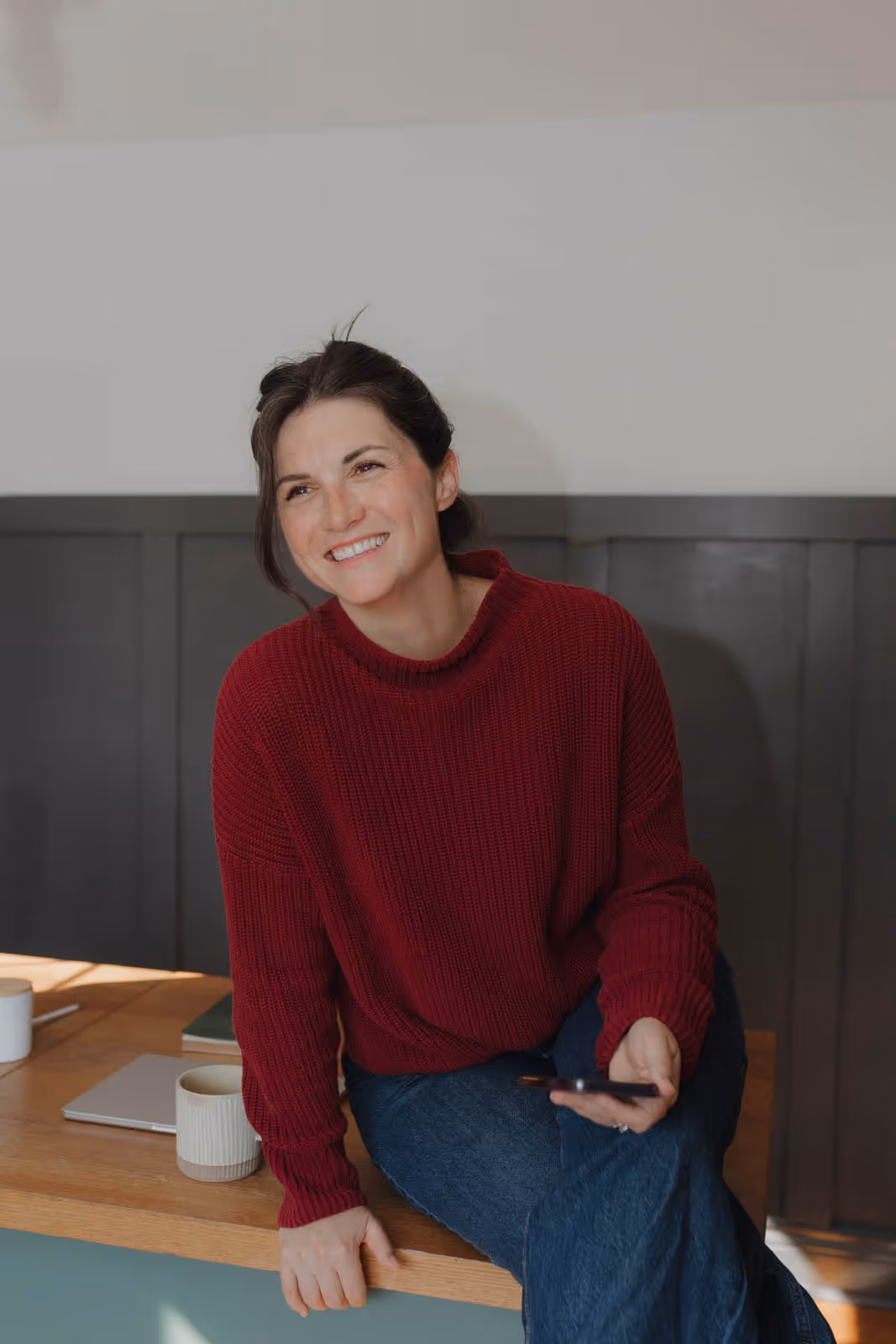 Devyn sitting on her office desk wearing a red sweater, smiling.