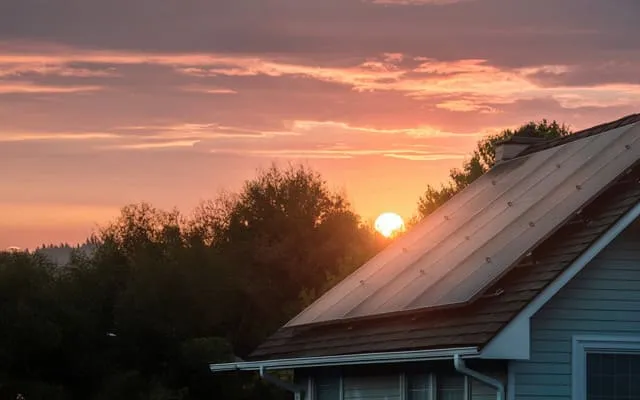 Solarmodule auf einem Hausdach bei Sonnenuntergang, mit einem warmen orange-roten Himmel im Hintergrund.