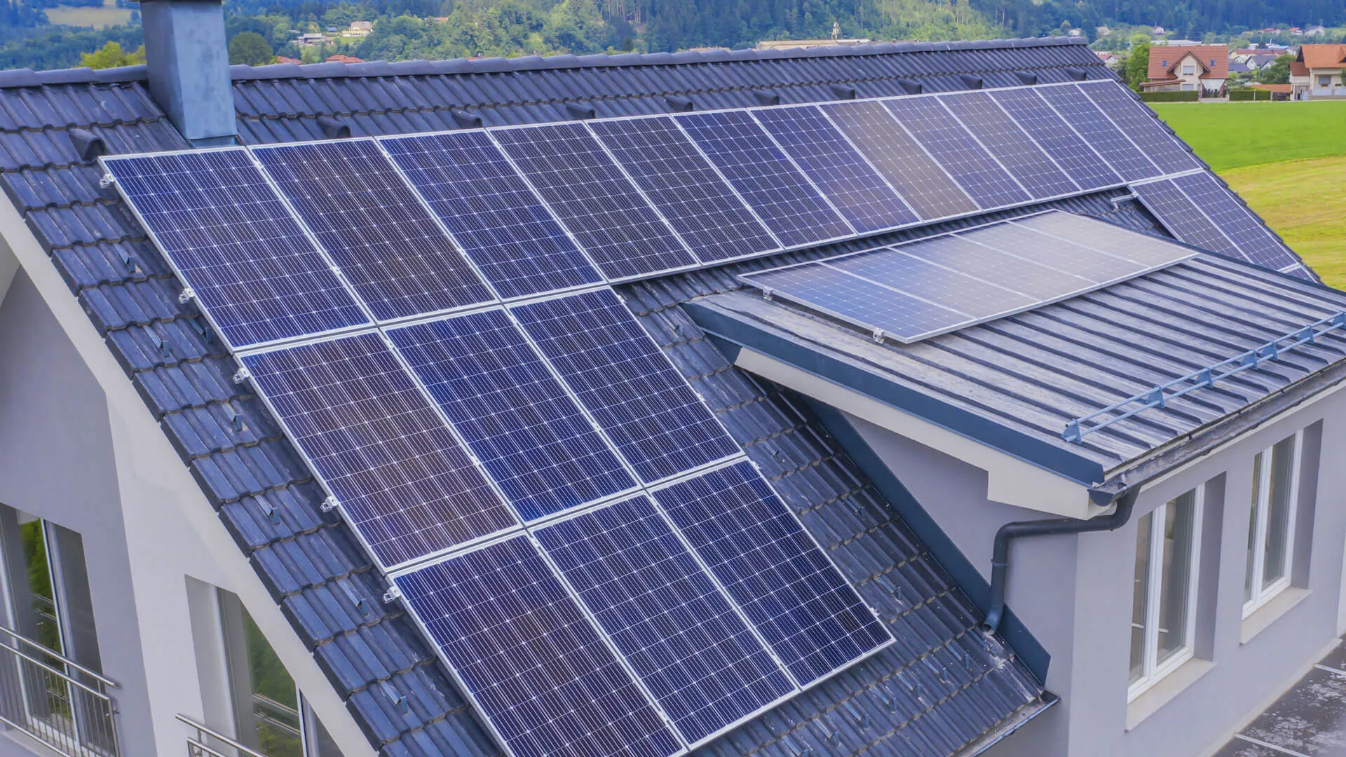 Ein modernes Wohnhaus mit einem dunklen Ziegeldach, auf dem großflächig Solarmodule installiert sind, im ländlichen Raum.