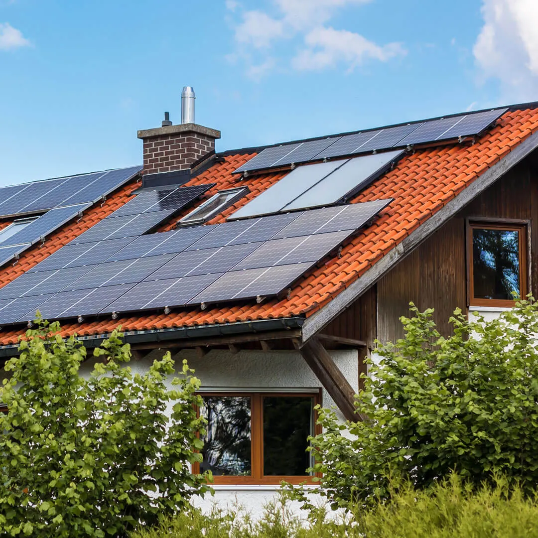 Ein Haus mit rotem Ziegeldach und mehreren installierten Solarmodulen unter blauem Himmel.