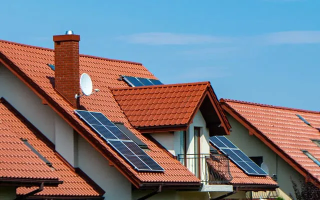 Eine Reihe von Häusern mit roten Ziegeldächern, auf denen Solarmodule installiert sind, unter einem klaren blauen Himmel.