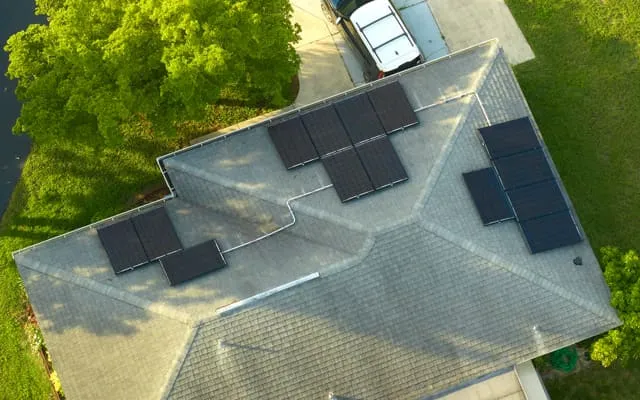Luftaufnahme eines Einfamilienhauses mit Solarmodulen auf dem Dach, umgeben von grünen Bäumen und Rasenflächen.