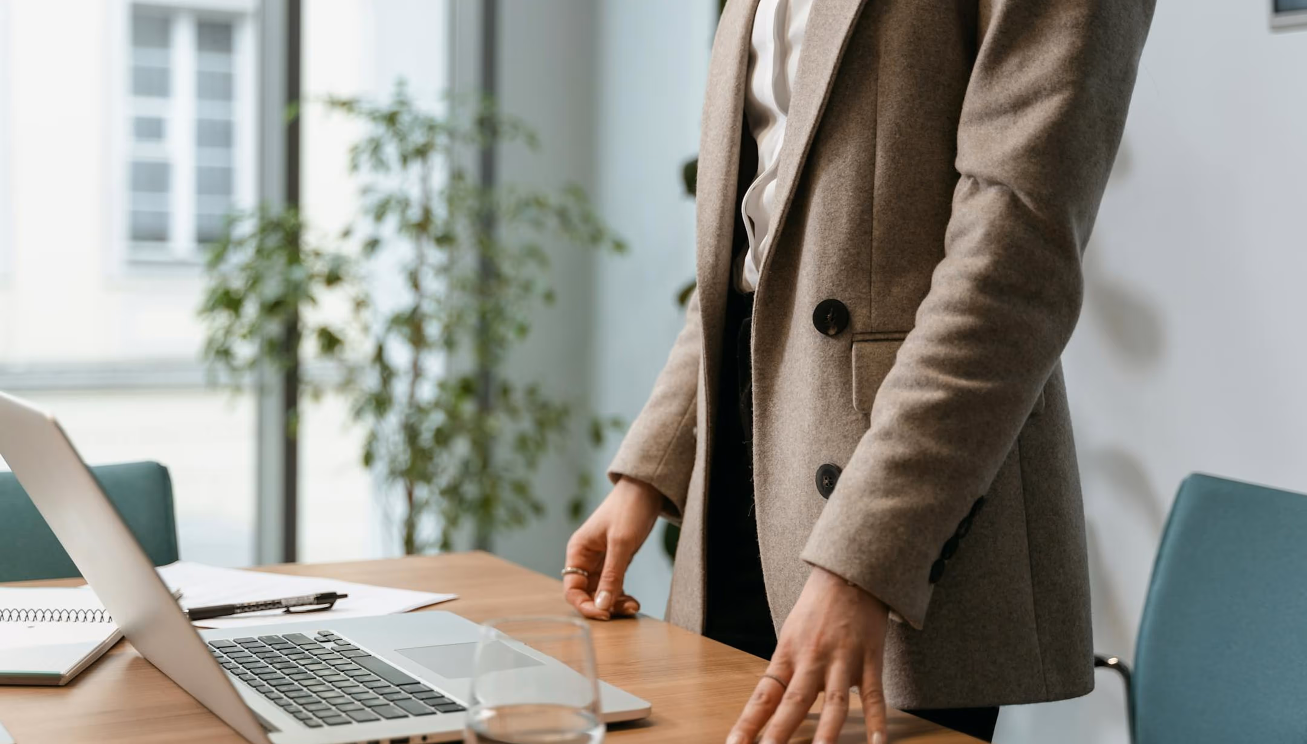 Professional standing at desk with laptop and notebook in modern office