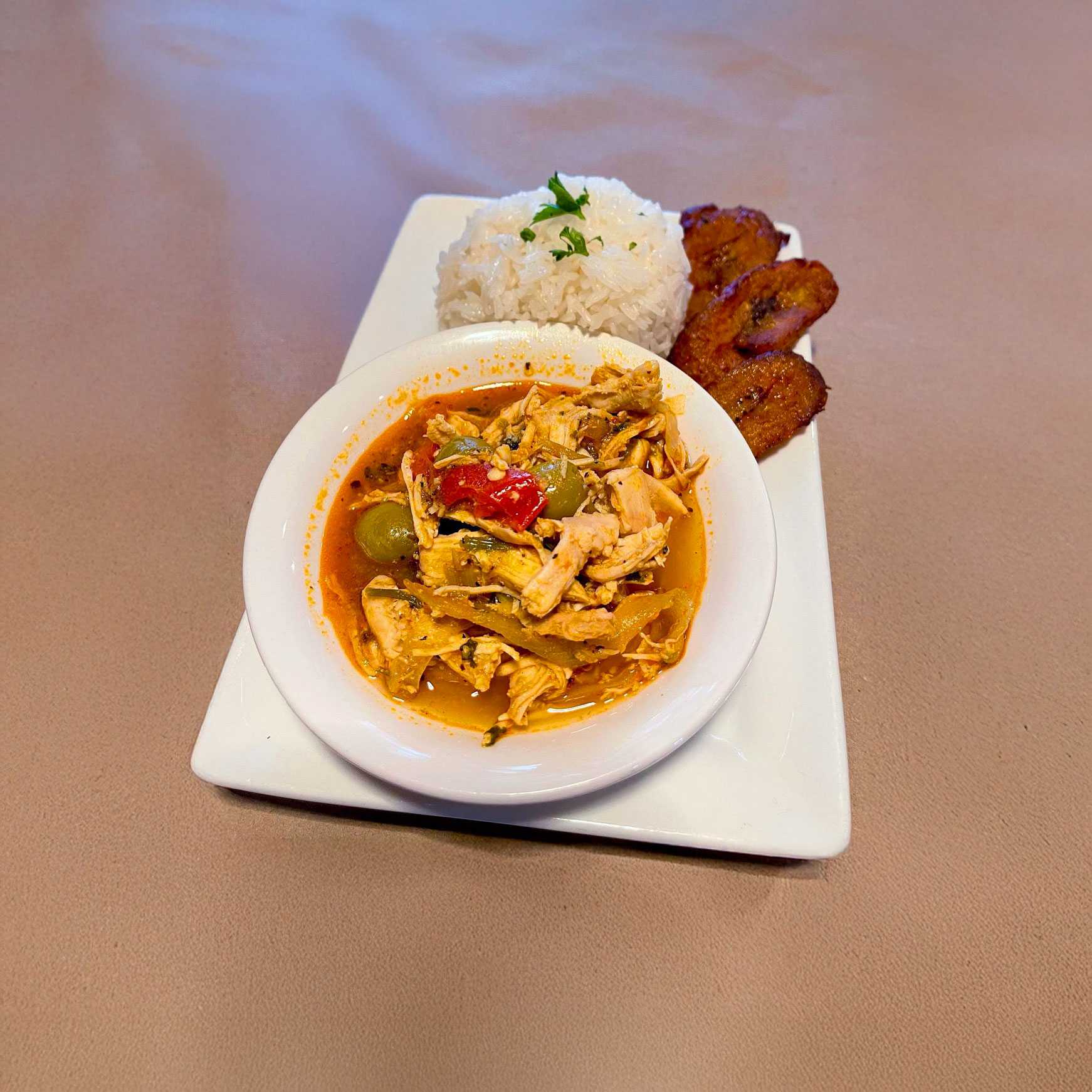 A plate of Chicken Ropa Vieja with rice and fried plantain slices.