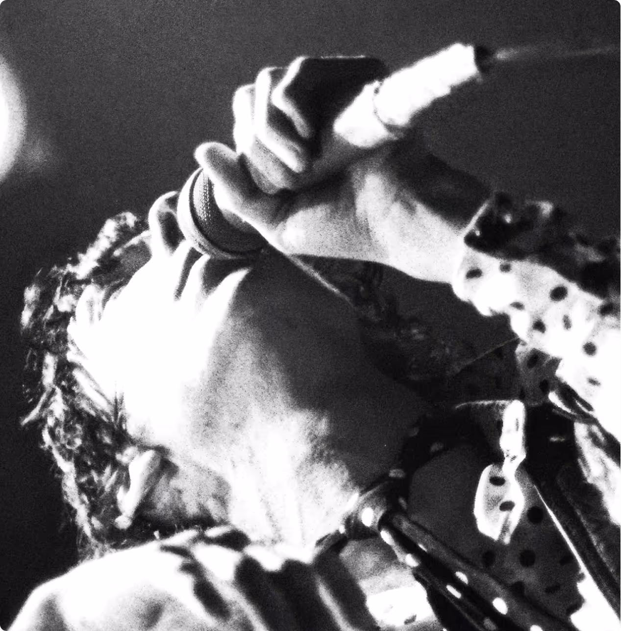 Close-up black and white photo of a man singing into a microphone with a polka dot shirt.
