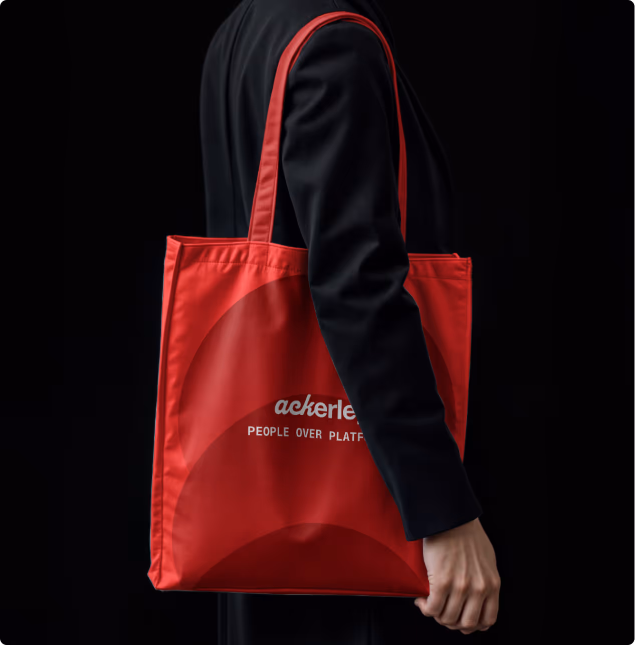 Person in black holding a red tote bag with text partially visible against black background.