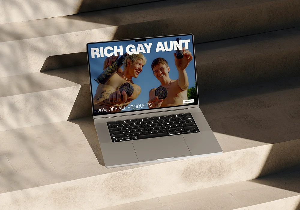 Open laptop on stone steps showing ad with two shirtless men holding skincare products.