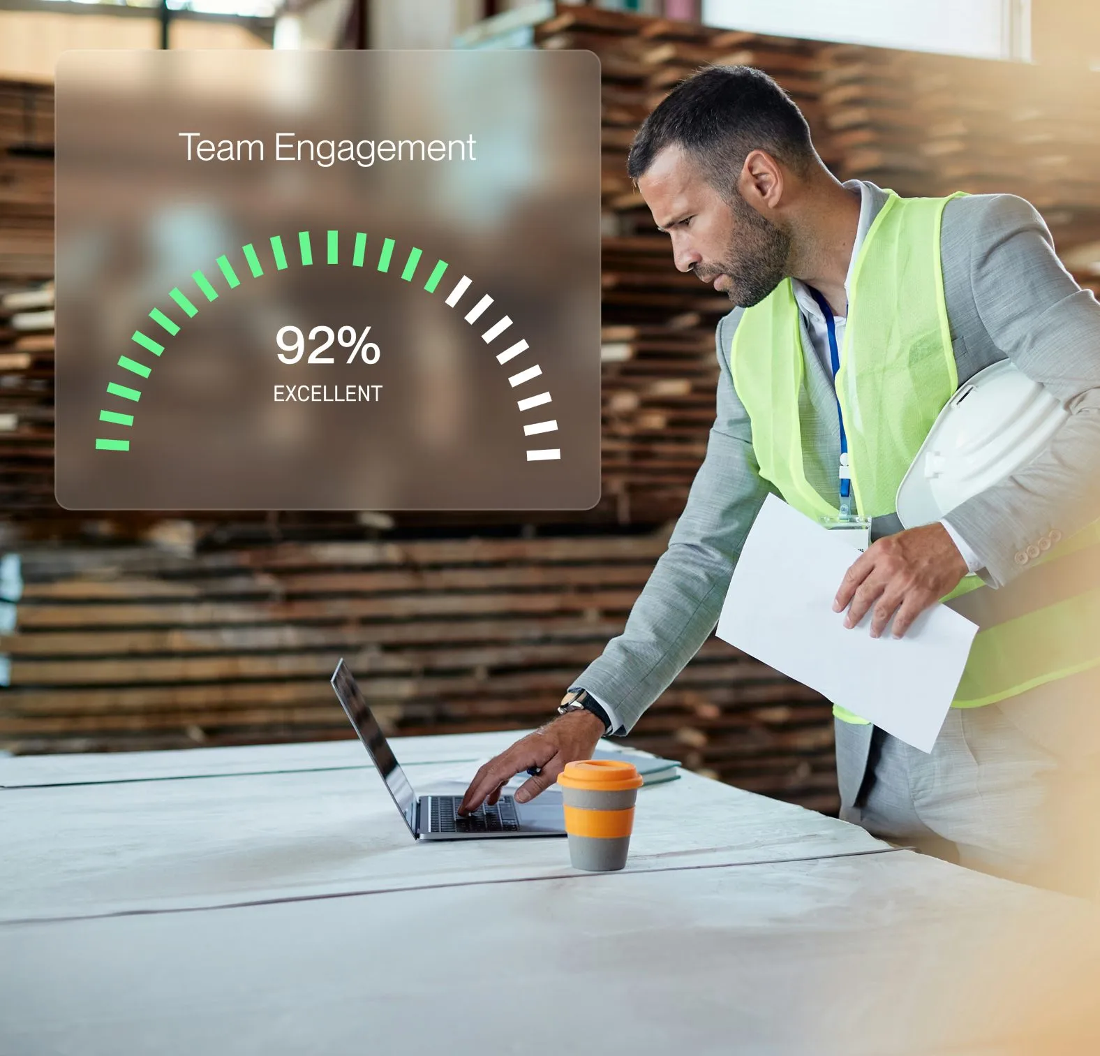 Man in a safety vest and suit checking a laptop on a table with a graphic overlay showing 92% team engagement labeled excellent.