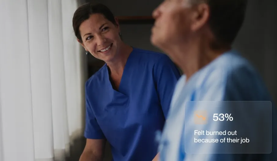 Smiling nurse talking with elderly patient wearing blue hospital gown near window.
