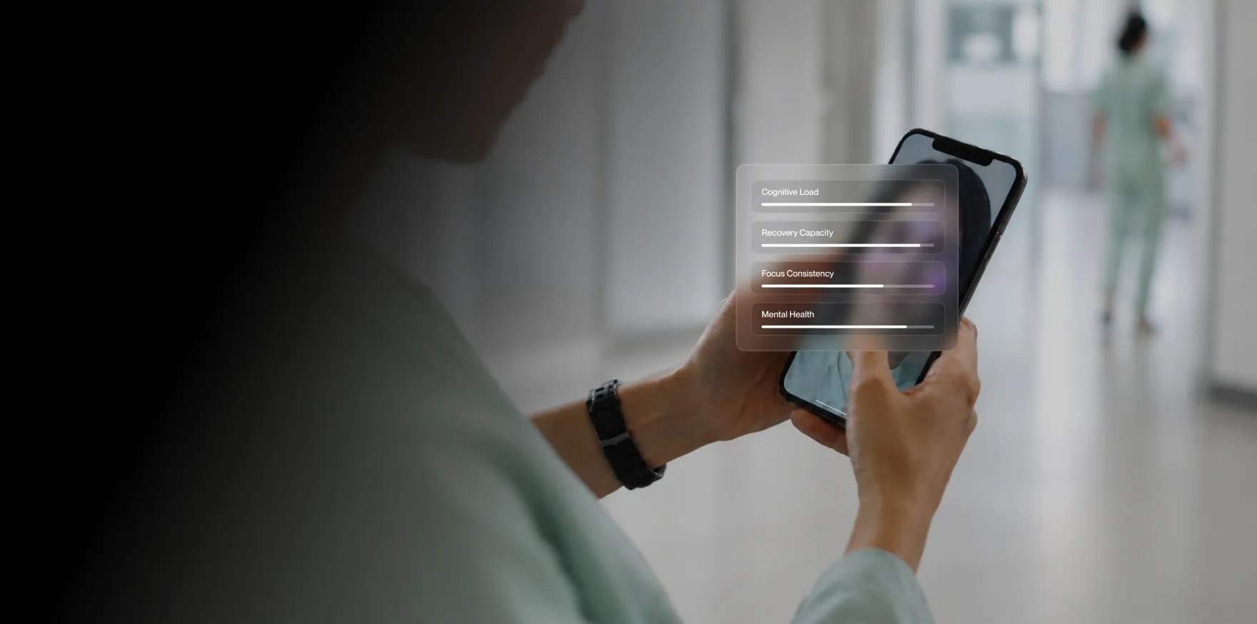 Person in scrubs holding smartphone showing mental health metrics including cognitive load and focus consistency.