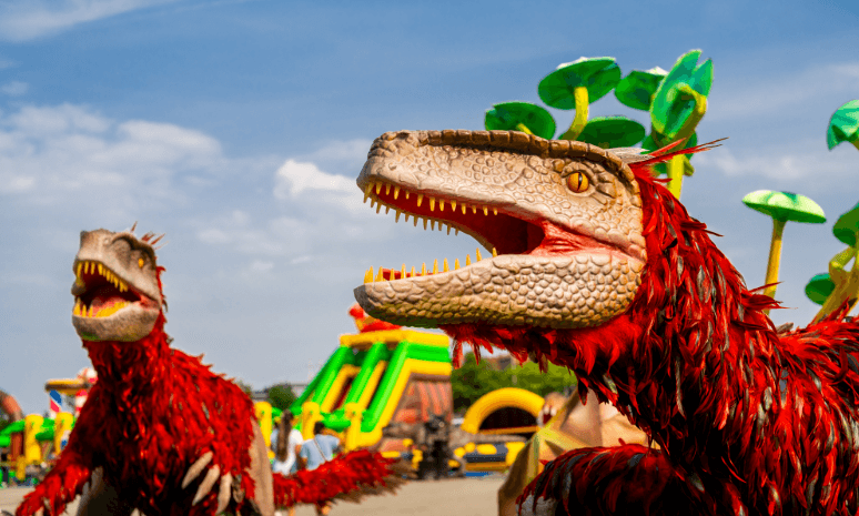 Two feathered animatronic Pyroraptor with vibrant red plumage displayed outdoors at LuminoCity Dino Safari.
