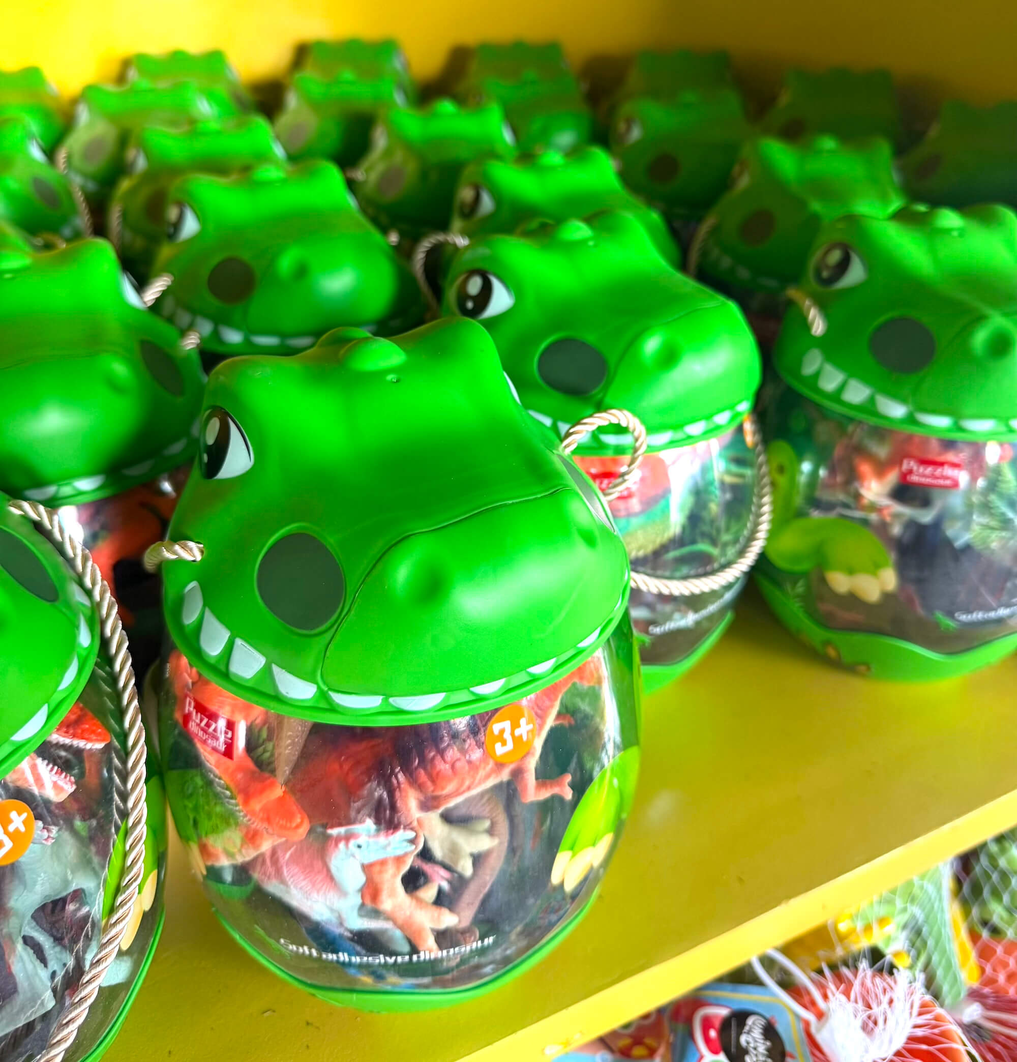 Green dinosaur head toy buckets filled with mini figures on display at the LuminoCity Dino Safari gift shop.