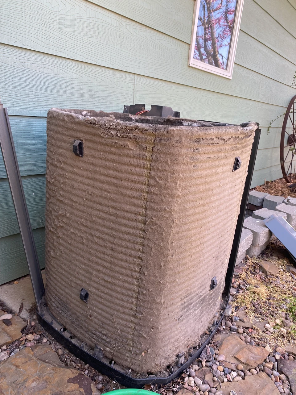 An aging, weathered outdoor AC condenser unit with bent cooling fins and dirt accumulation An aging, weathered outdoor AC condenser unit with bent cooling fins and dirt accumulation