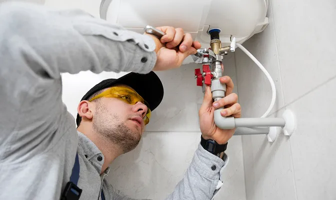 A man wearing yellow safety glasses, focused on repairing a water heater.