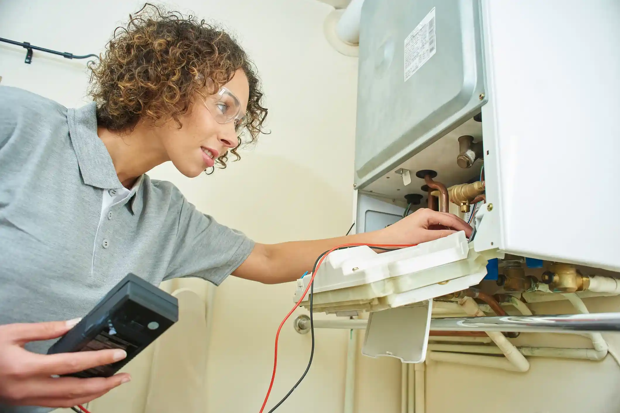 Female technician wearing safety glasses examining the internal wiring of a boiler.