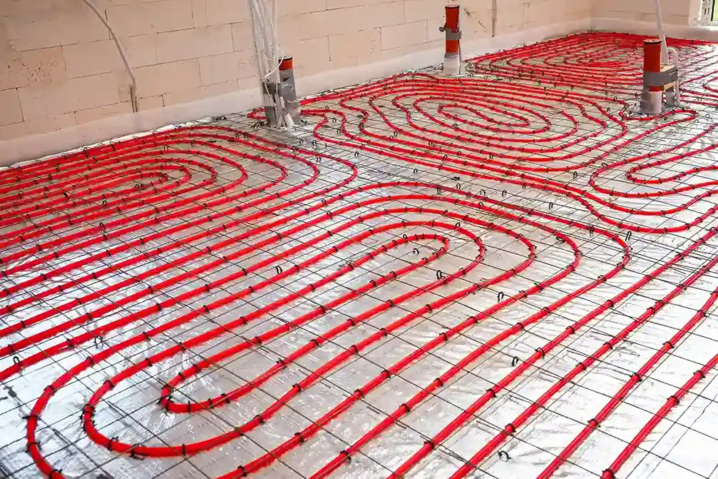 A construction site view of a floor with red radiant heating pipes arranged in spiral and looping patterns on a shiny gray floor mat.