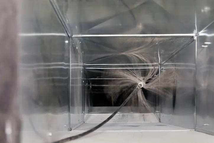 A view from inside a clean, rectangular metal air duct as a tool with a spray of wires cleans it.