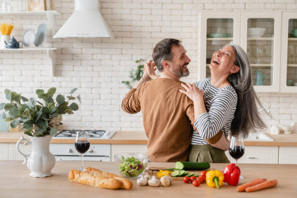 smiling oder couple dancing togetherand cooking in kitchen; long grey hair flowing